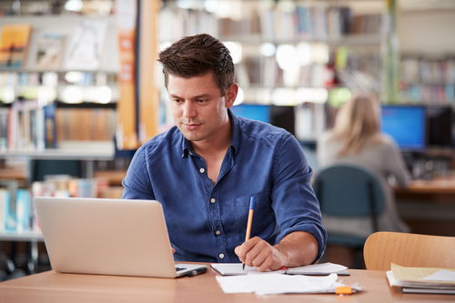 Student in blue shirt studying in front of laptop
