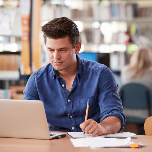 Student in blue shirt studying in front of laptop