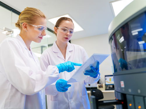Deux femmes vêtues de blouses blanches et portant des lunettes de protection devant des flacons de produits chimiques