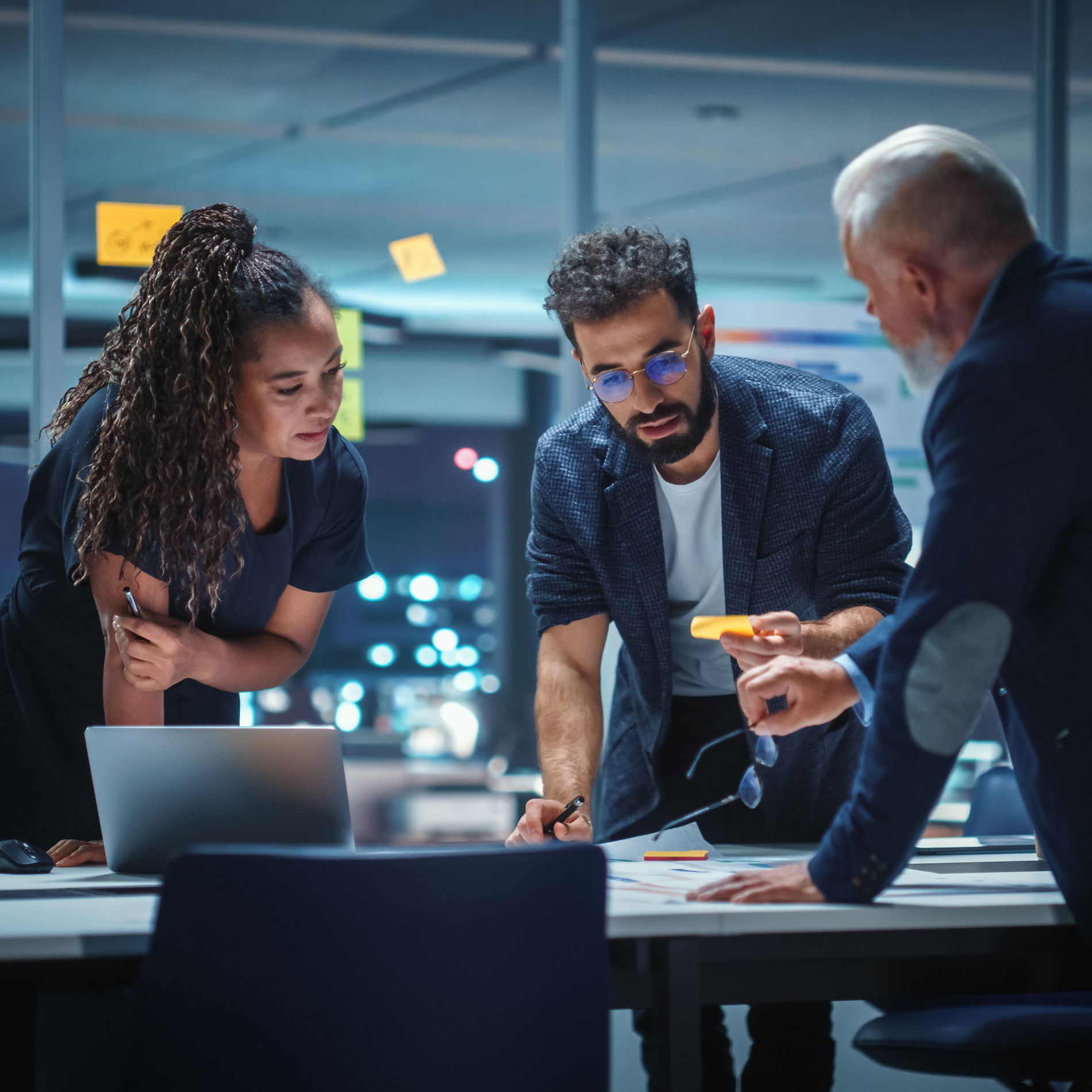 A woman and two men are leaning over a table discussing a piece of paper