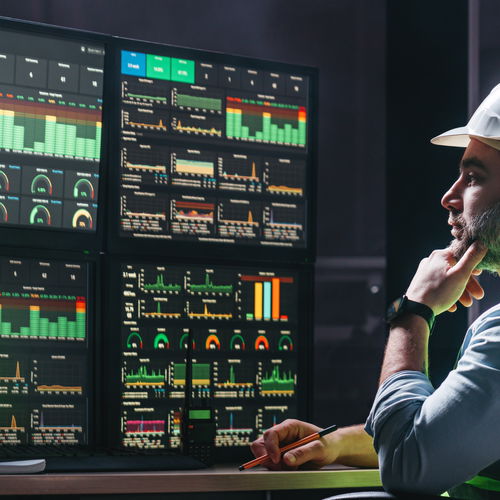 Workers wearing helmets and vests in front of monitors full of statistics