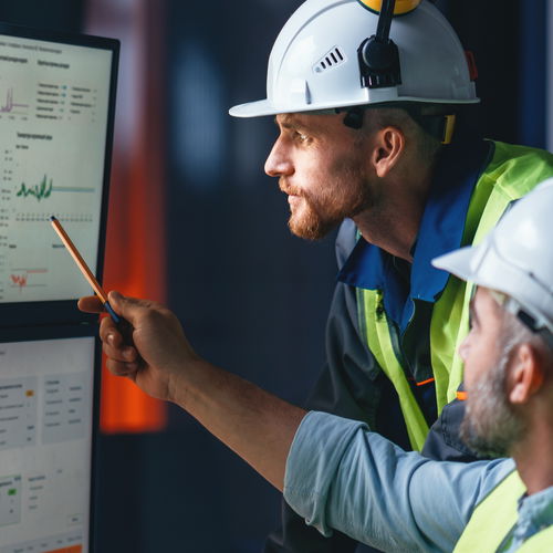 Workers wearing helmets and vests in front of monitors
