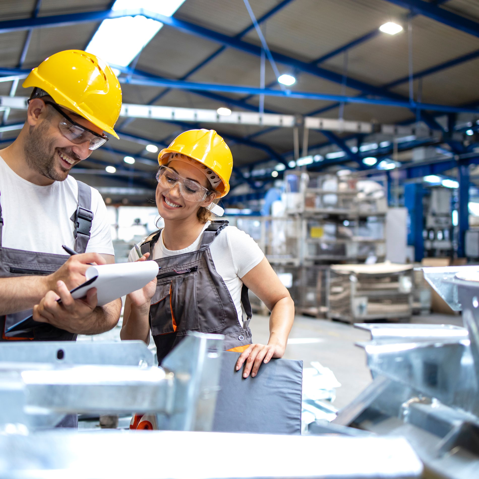 Workmen wearing helmets look at a piece of paper in an industrial hall.