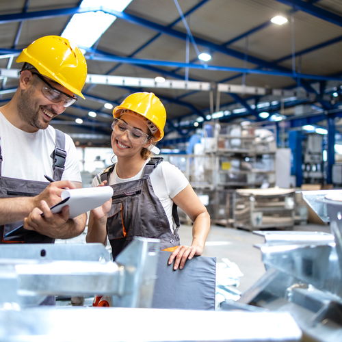 Workmen wearing helmets look at a piece of paper in an industrial hall.