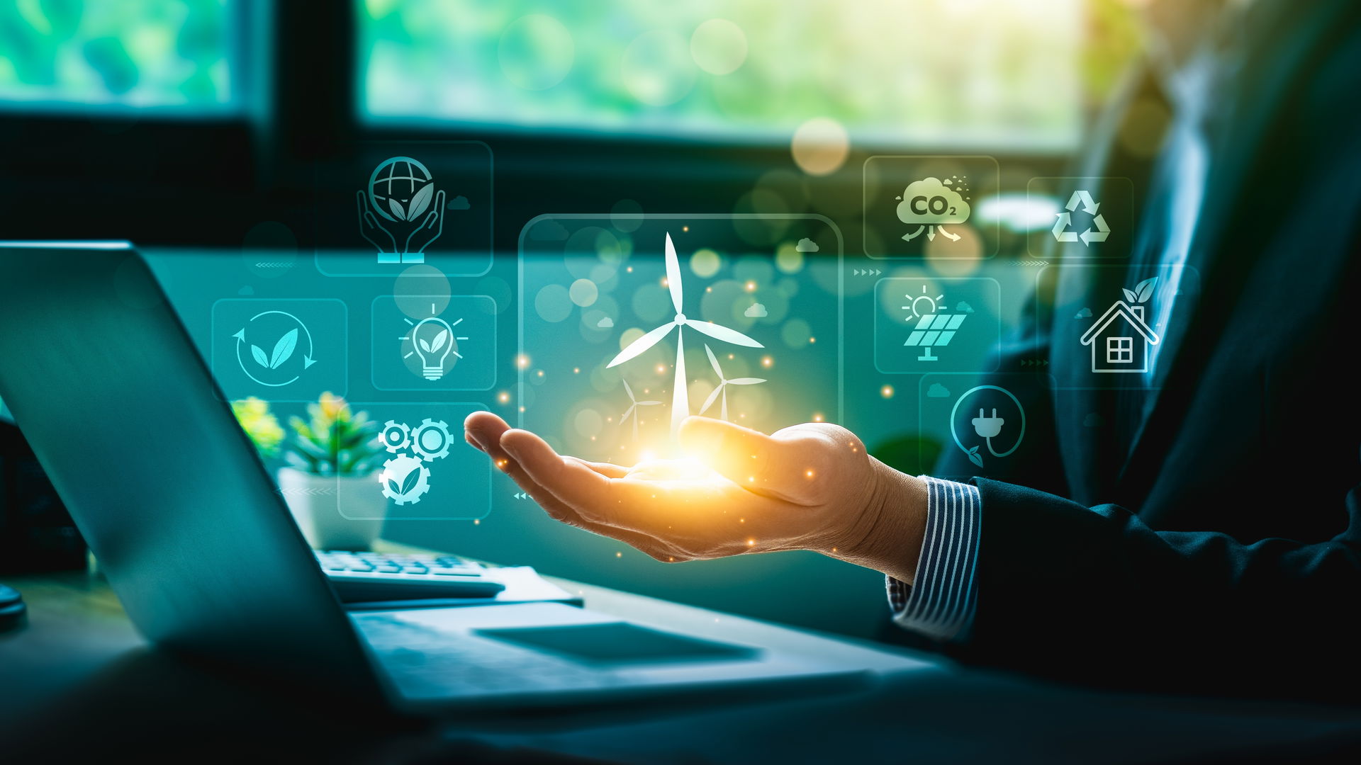 Hand holding a glowing ball with a windmill in front of a computer